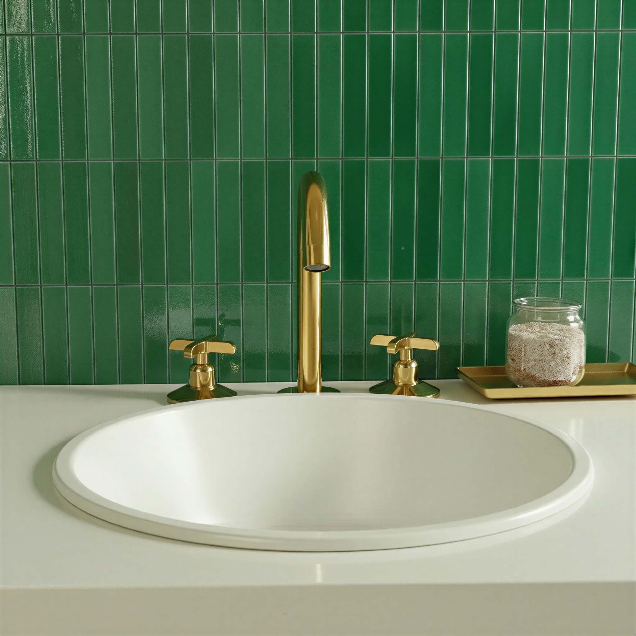 Bathroom sink with gold faucet and handles against a green tiled wall.
