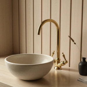 Bathroom setup with a white sink, gold faucet, and black vase against a wooden panel wall.