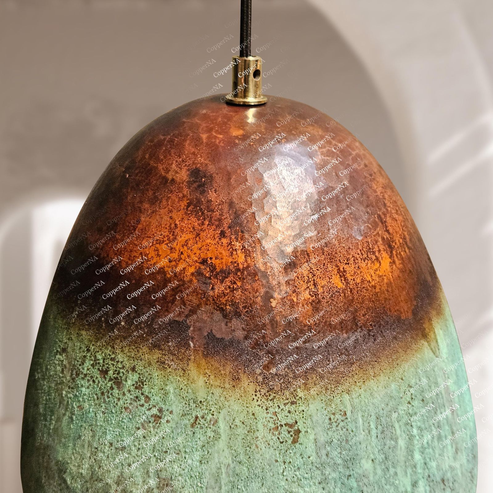 An egg-shaped pendant light with a glossy ceramic finish, featuring a rustic color gradient from coppery orange at the top to a textured green at the bottom, with a brass metal cap and black hanging cord.