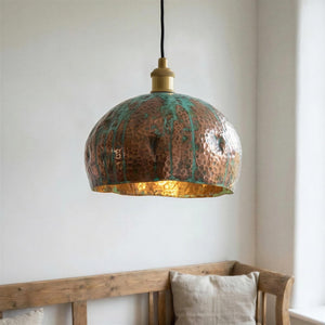 Copper pendant light with green patina hanging above a wooden bench.