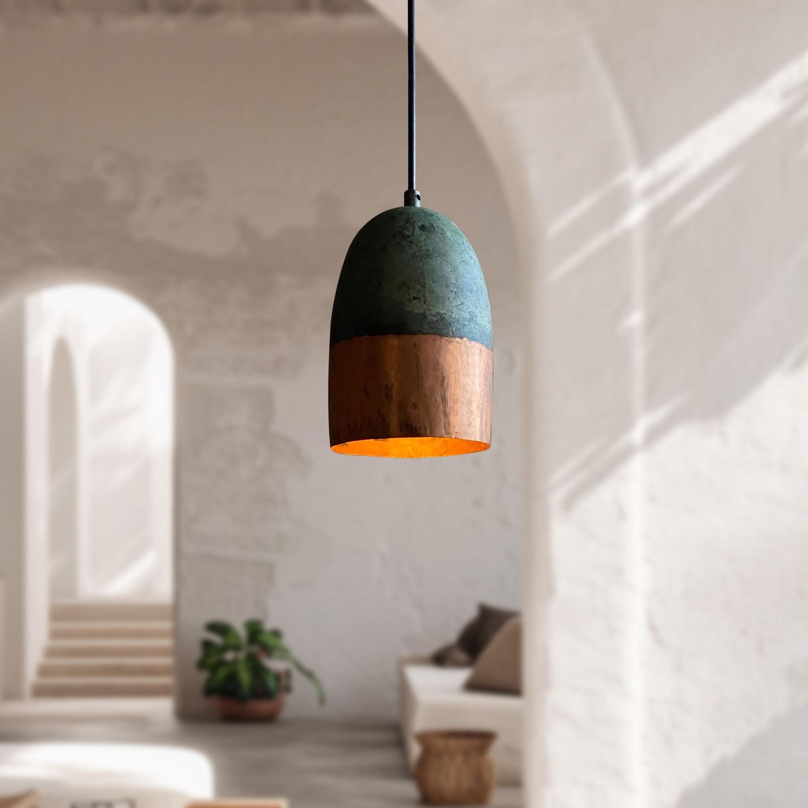 Pendant light with green top and copper bottom in a blurred room setting