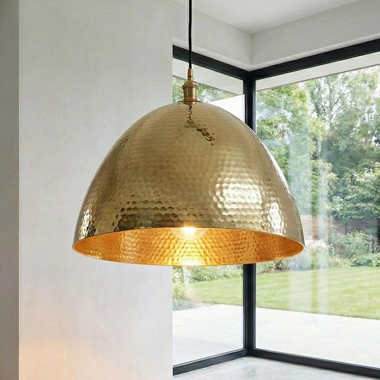 Gold pendant lamp hanging in a room with large windows showing greenery outside