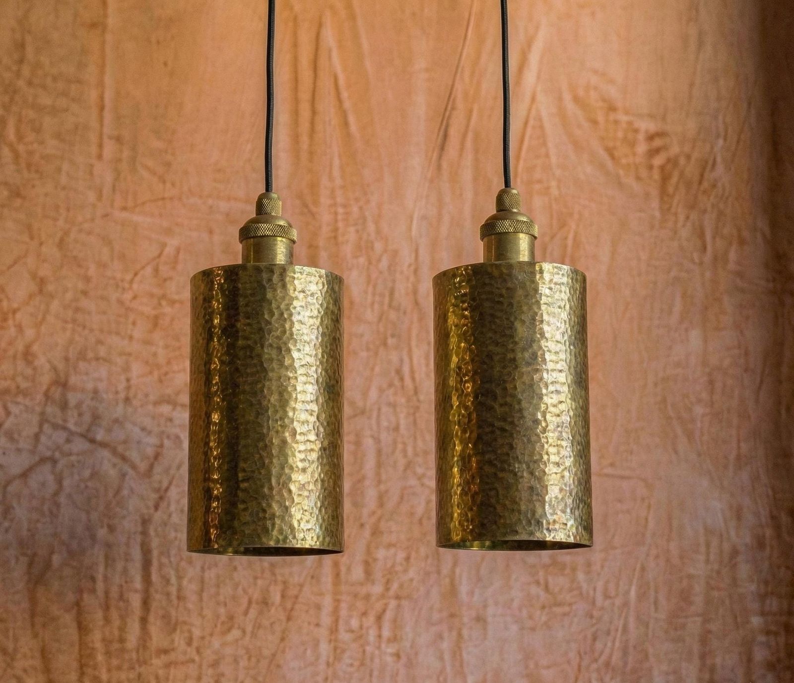 Two brass pendant lights hanging against a textured brown wall.