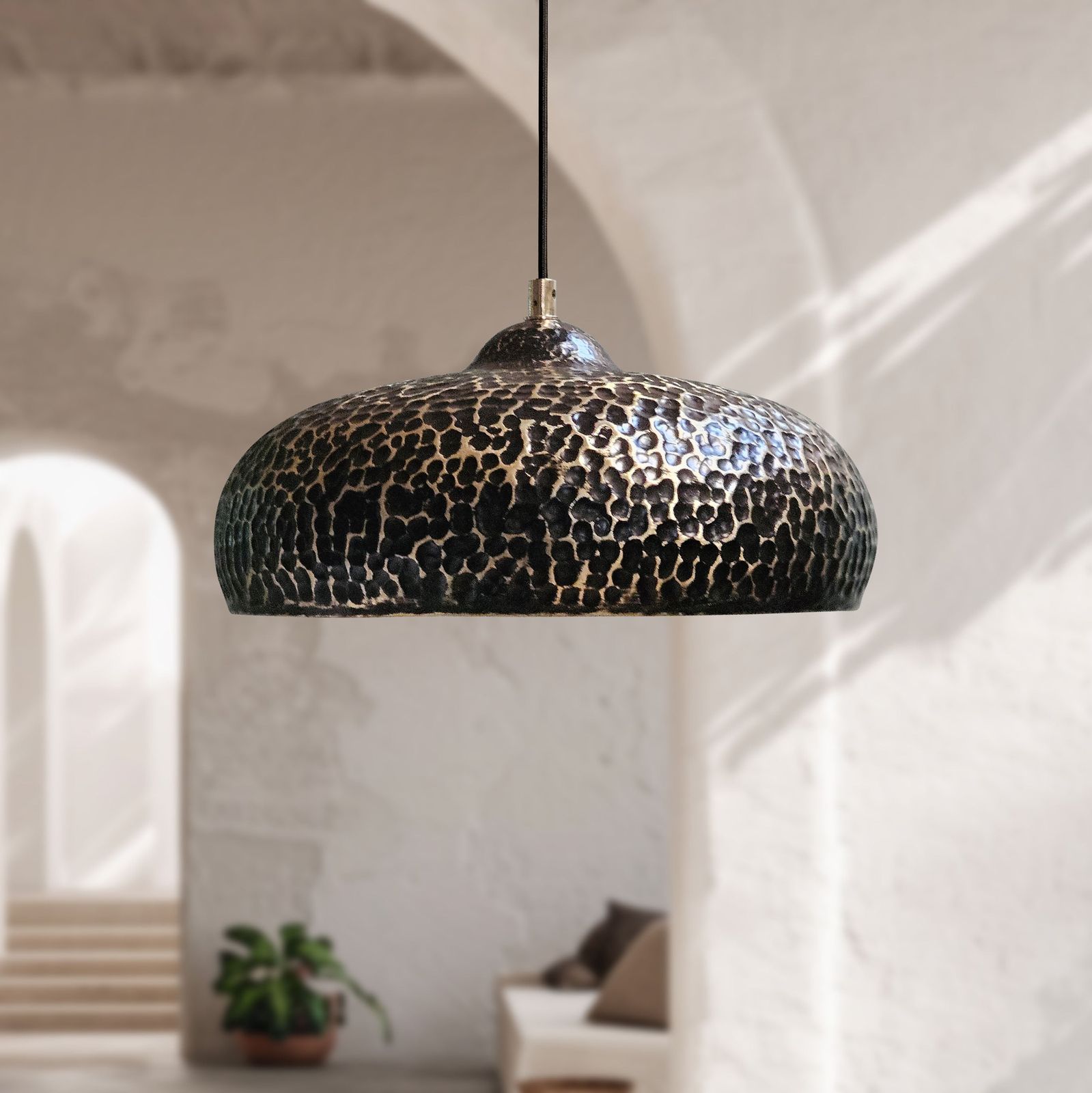 Hammered black and brass dome pendant light hanging in a bright, modern minimalist room with arched doorways.