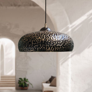 Hammered black and brass dome pendant light hanging in a bright, modern minimalist room with arched doorways.