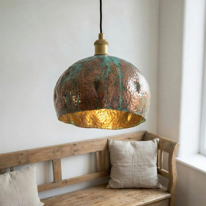 Copper pendant light hanging above a wooden bench with pillows in a room.