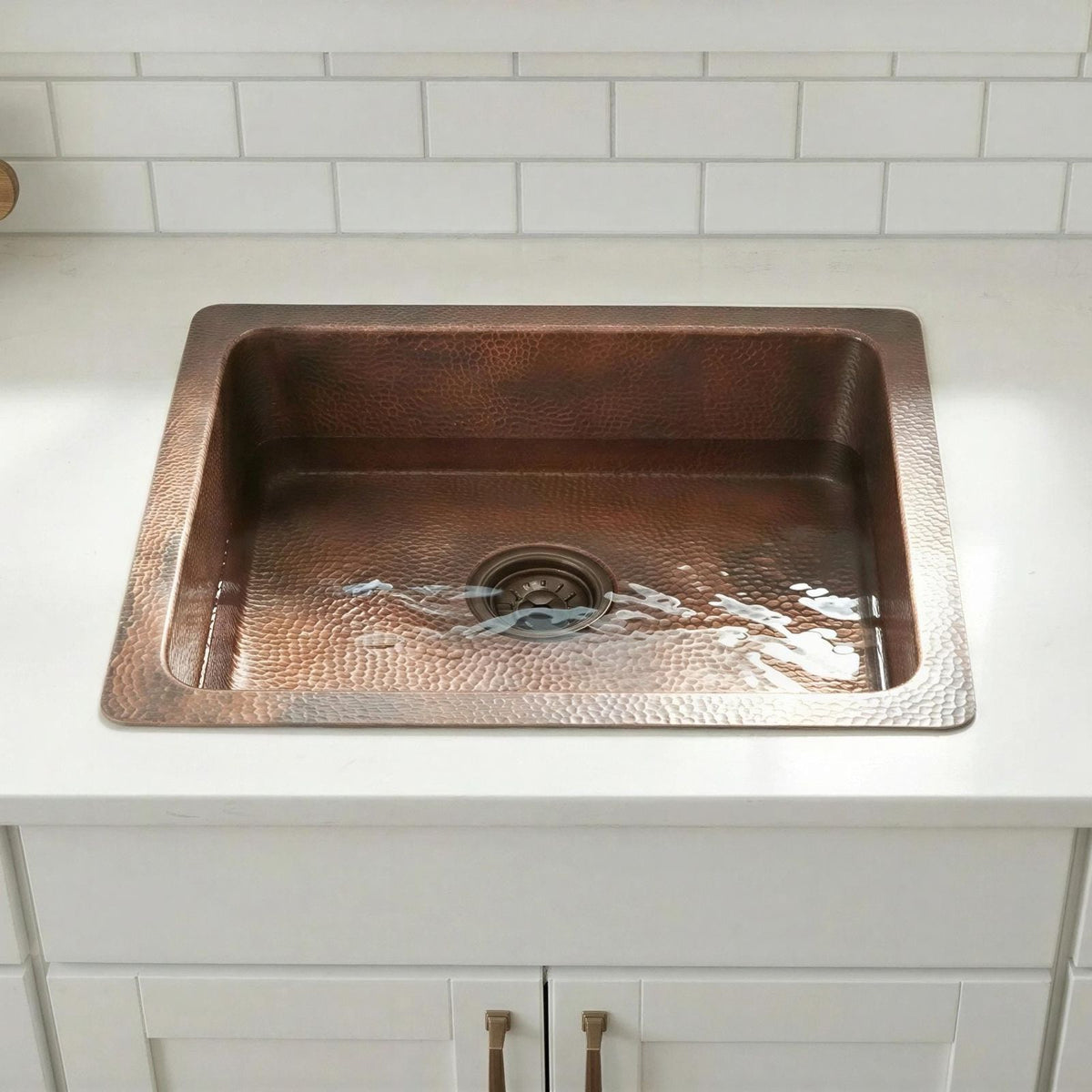 Copper kitchen sink on a white countertop with tiled wall background