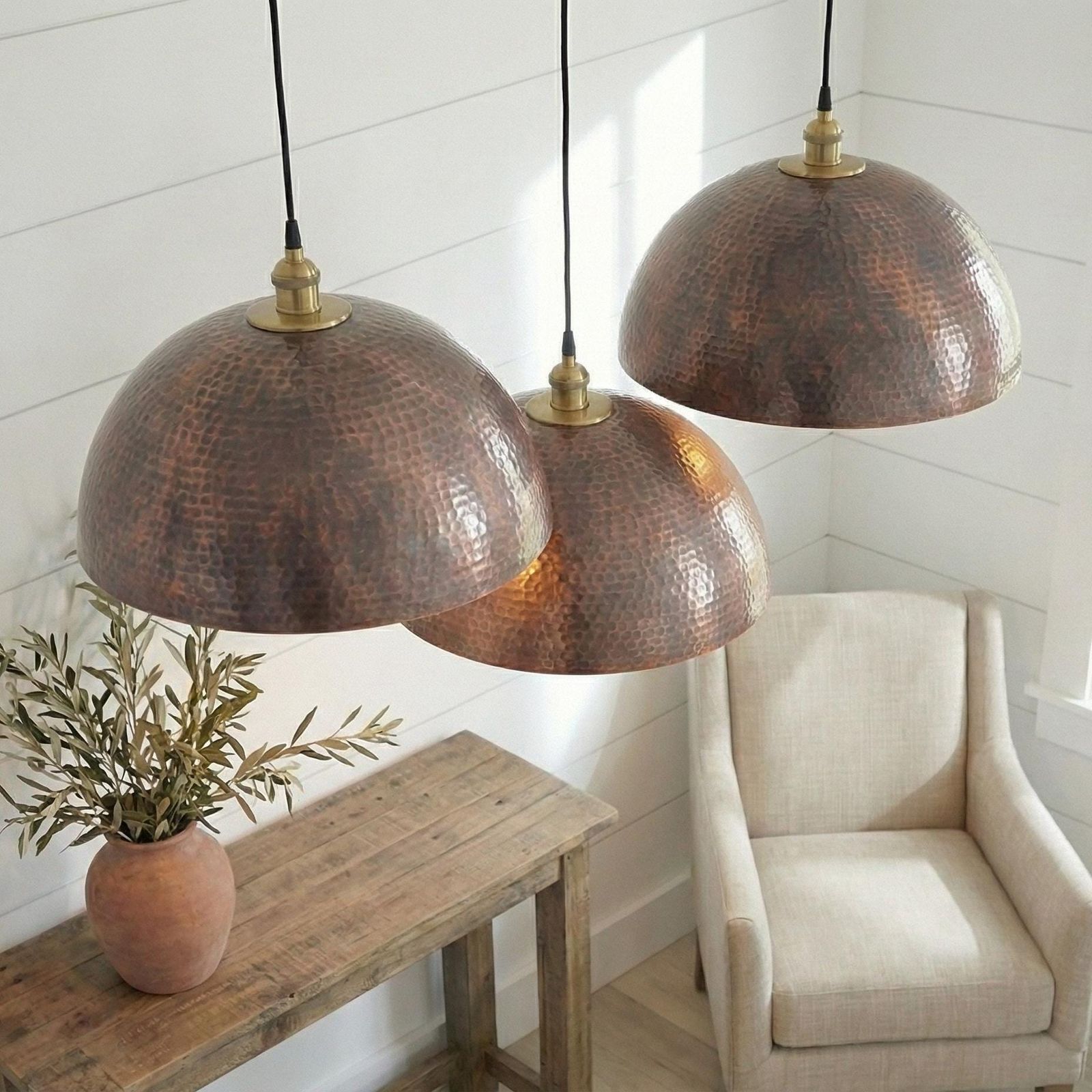 Three copper pendant lights hanging in a room with a wooden table and chair.