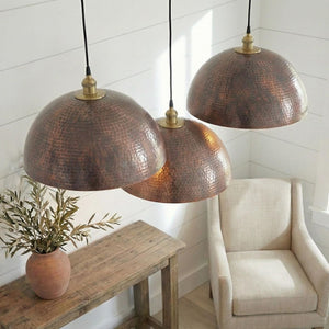 Three copper pendant lights hanging in a room with a wooden table and chair.