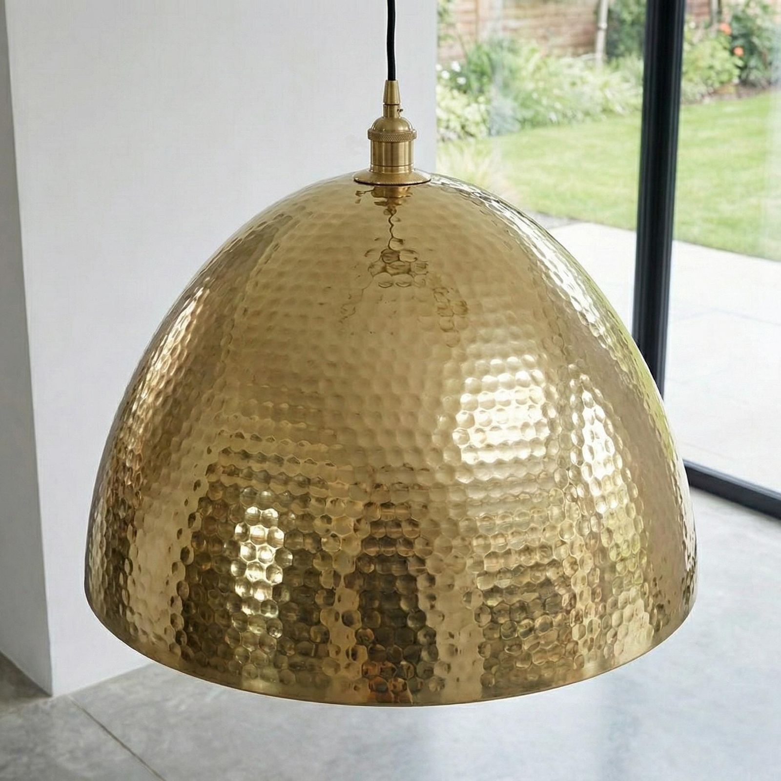 Gold pendant light with a textured surface in a room with a window.