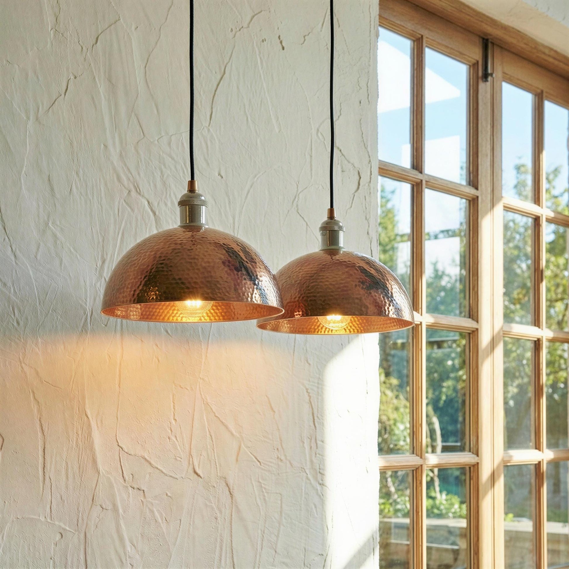 Two copper pendant lights hanging in a room with a window in the background.