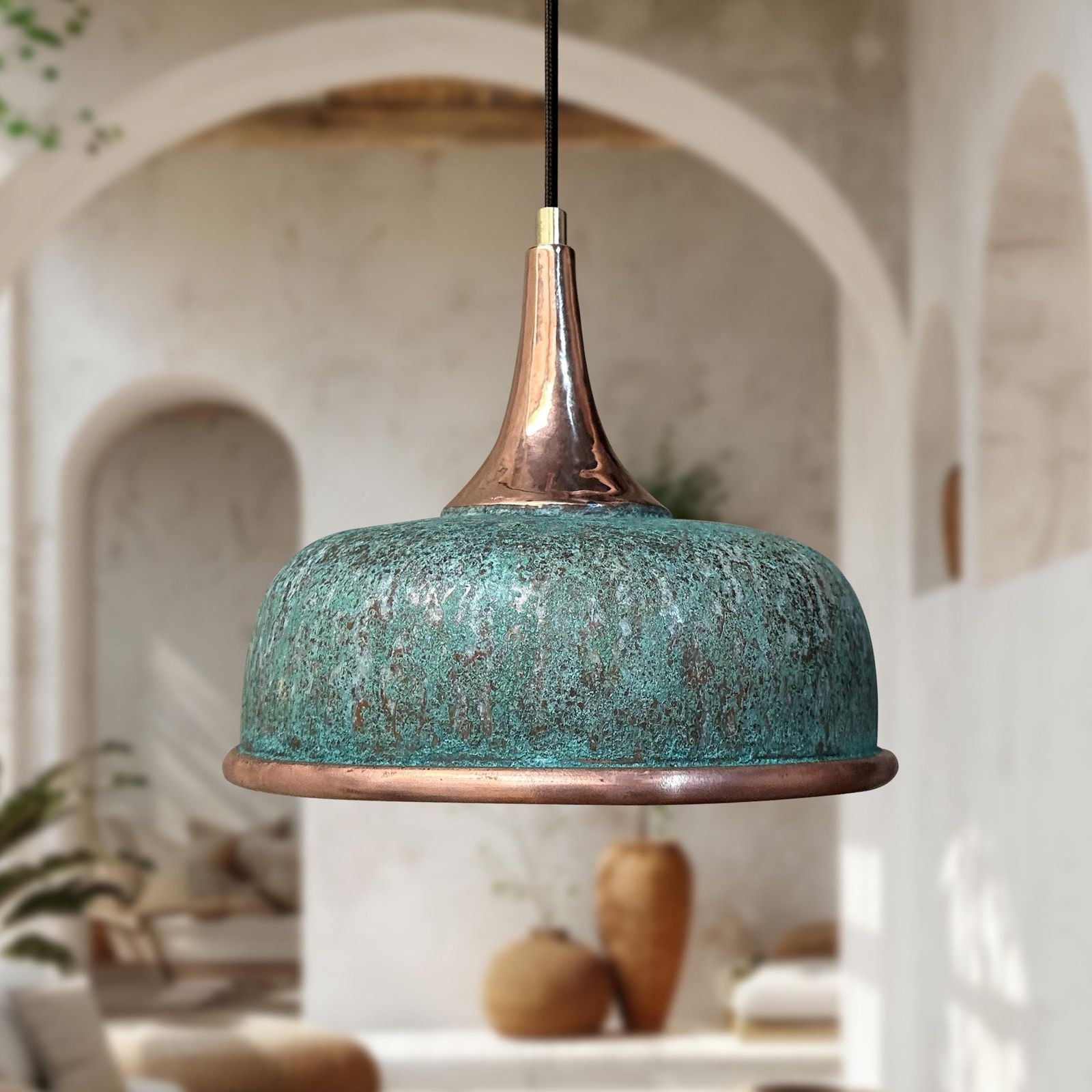 Turquoise pendant light with copper accents hanging in a room with arches and plants.