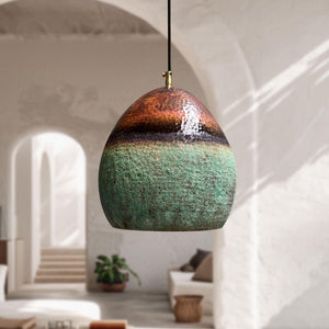 Decorative pendant light with a textured design hanging in a room with white walls and a plant.