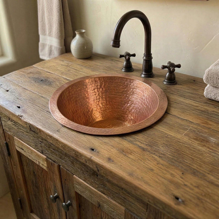 Copper sink on a wooden countertop with a rustic cabinet and decorative elements.