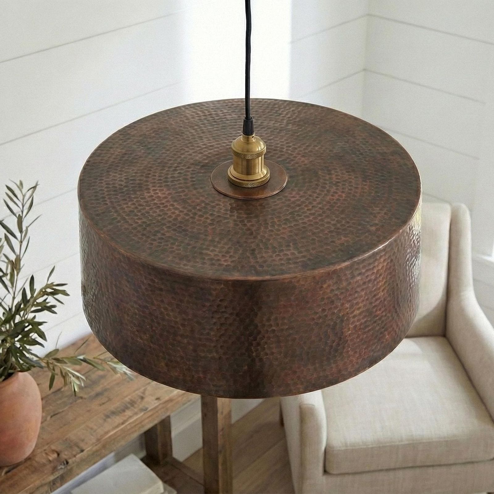Copper pendant light fixture on a wooden stand with a plant and sofa in the background.