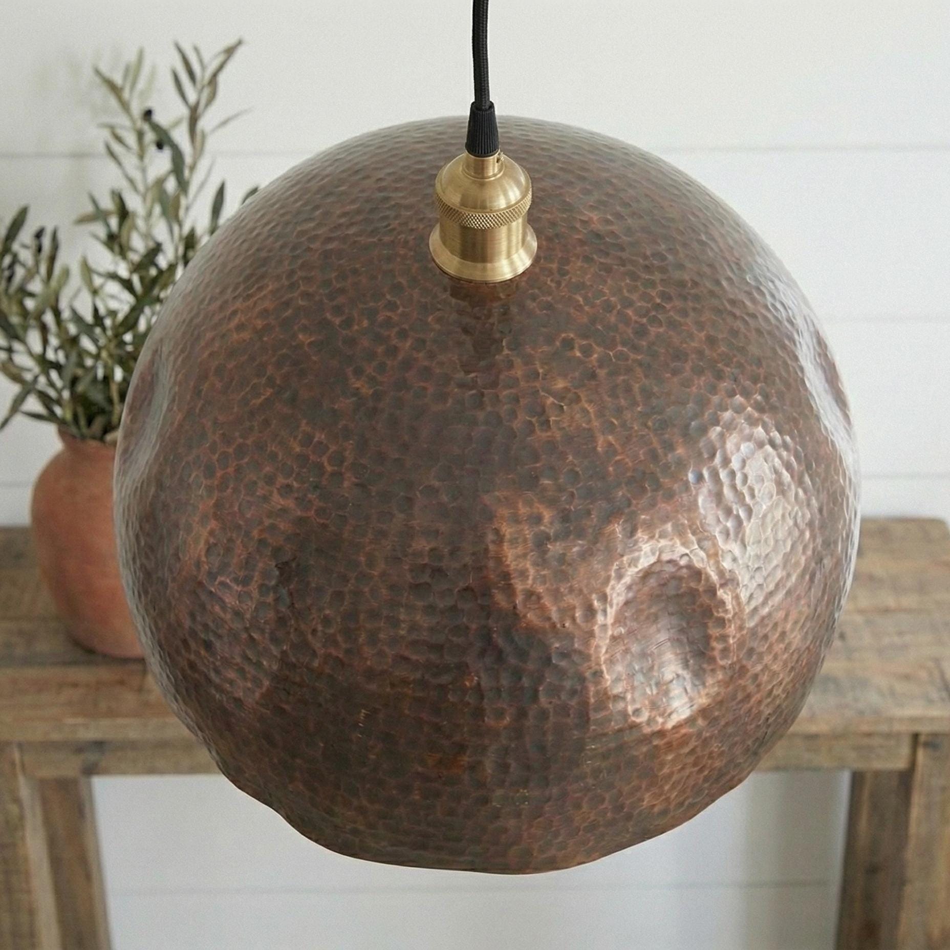 Hammered copper pendant light on a wooden table with a plant in the background