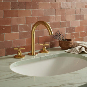 Gold faucet on a marble sink with a tiled wall background