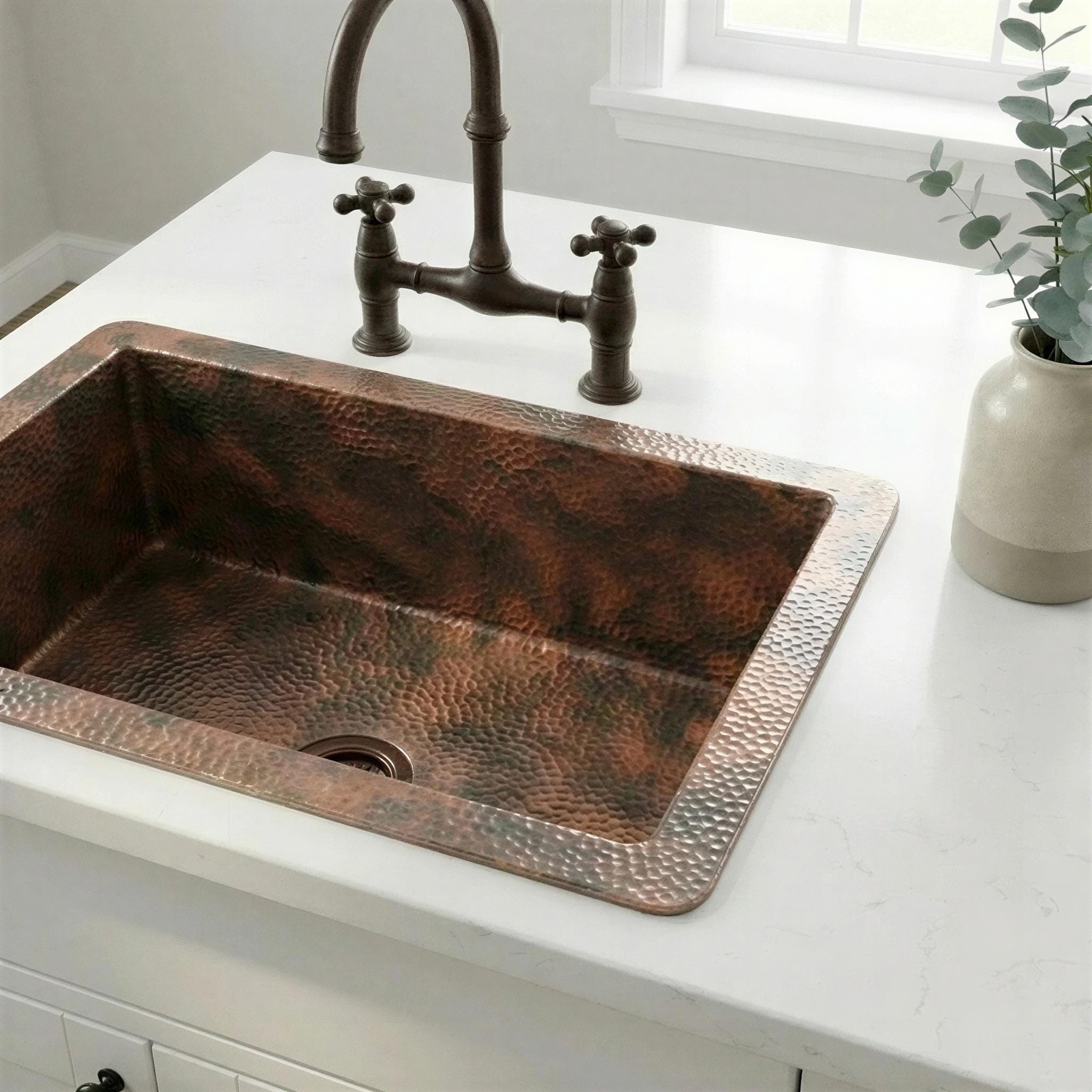 Copper kitchen sink with rustic faucet on a white countertop