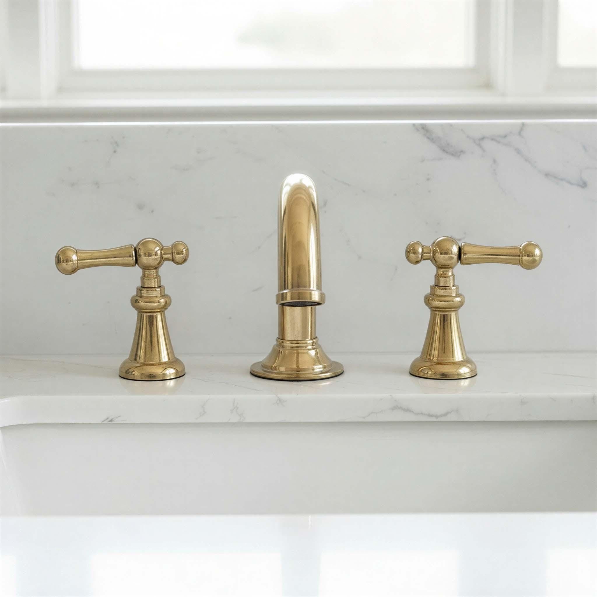 Brass faucet set on a marble countertop with a window in the background