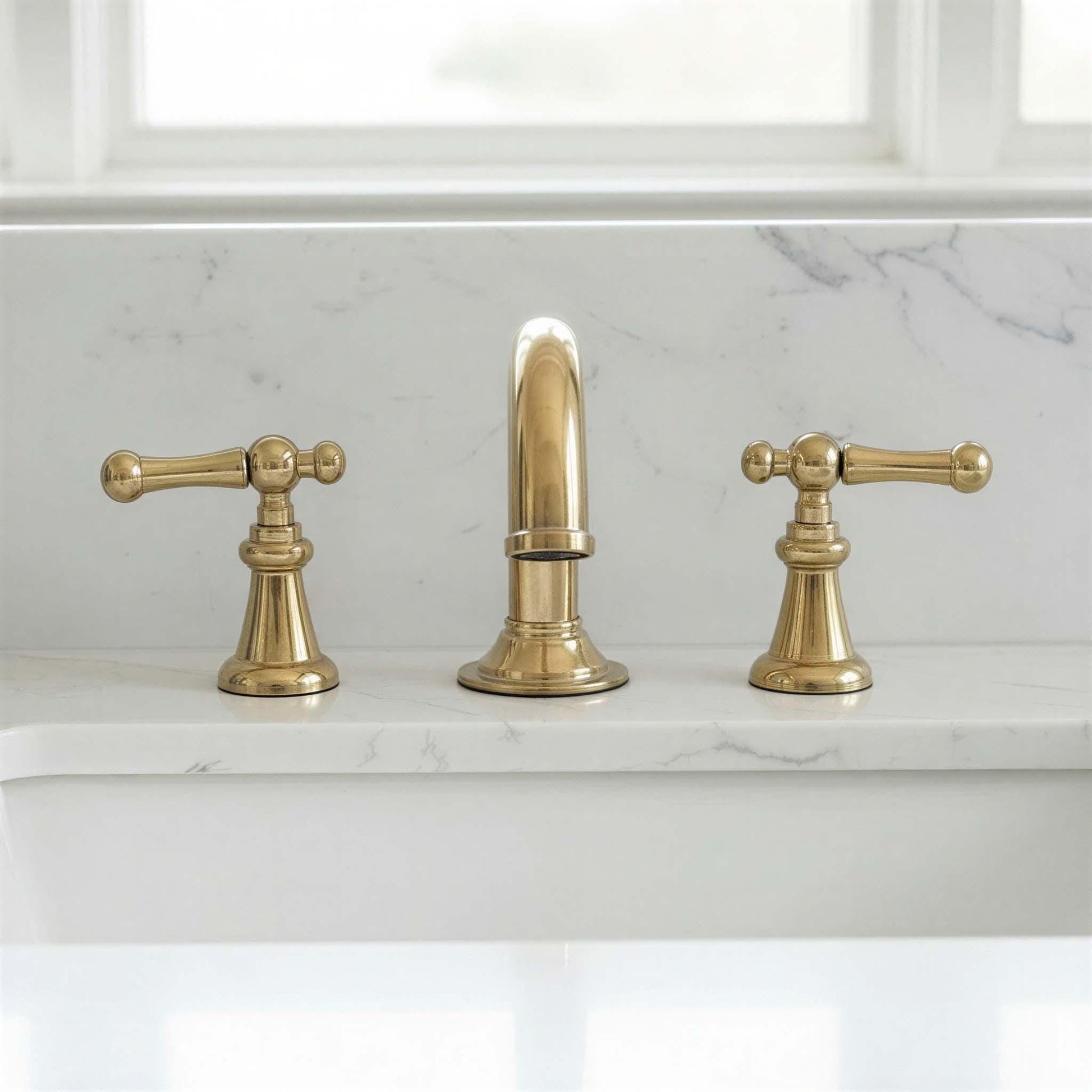 Brass faucet set on a marble countertop with a window in the background