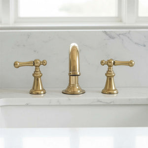 Brass faucet set on a marble countertop with a window in the background