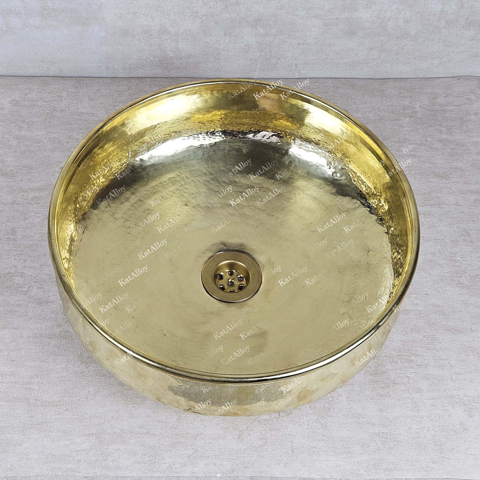 Gold-colored round basin with central drain on a gray background