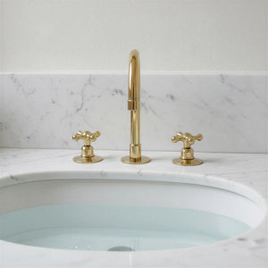 Gold faucet and handles on a white sink with marble backsplash