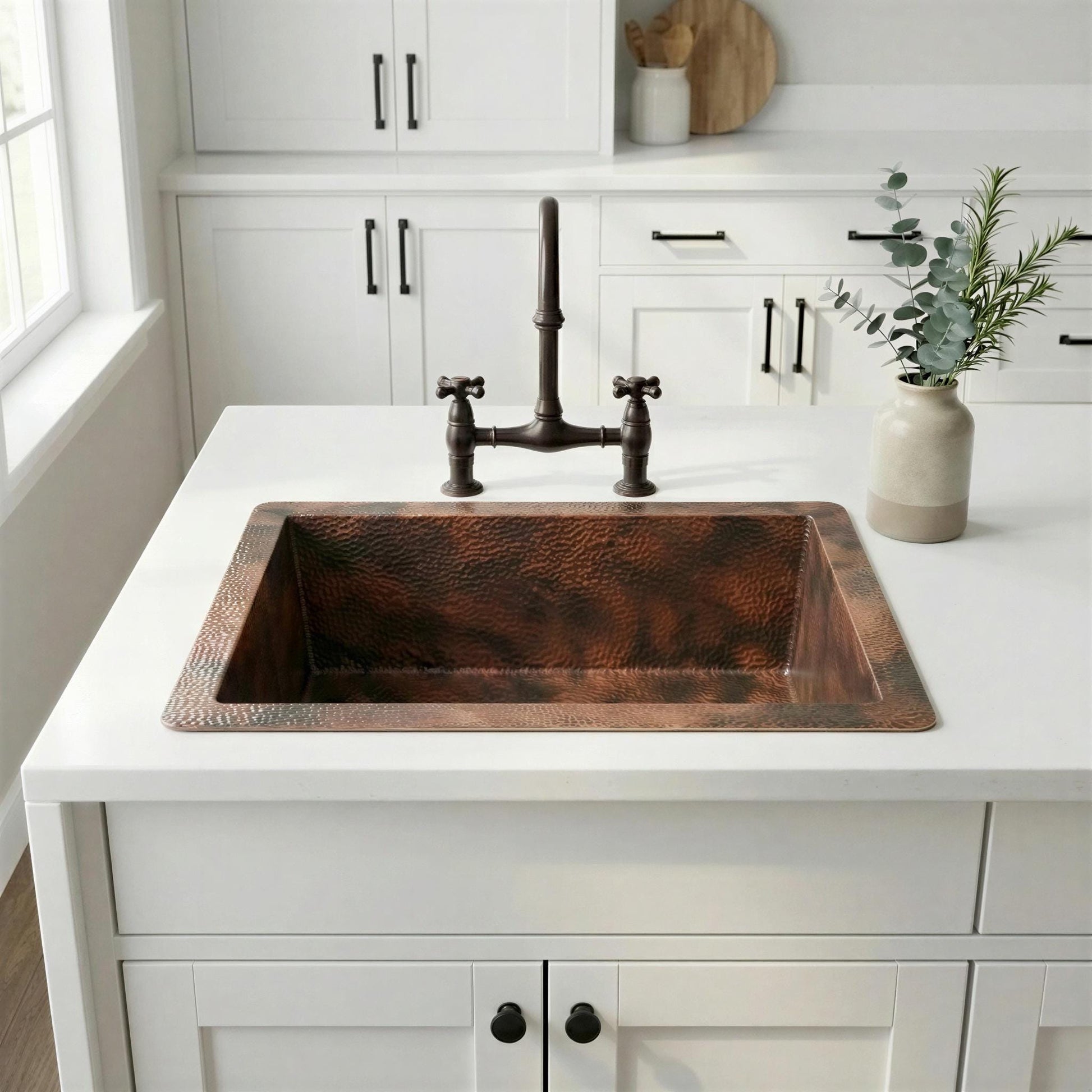 Copper kitchen sink on a white countertop with white cabinets and a window in the background.