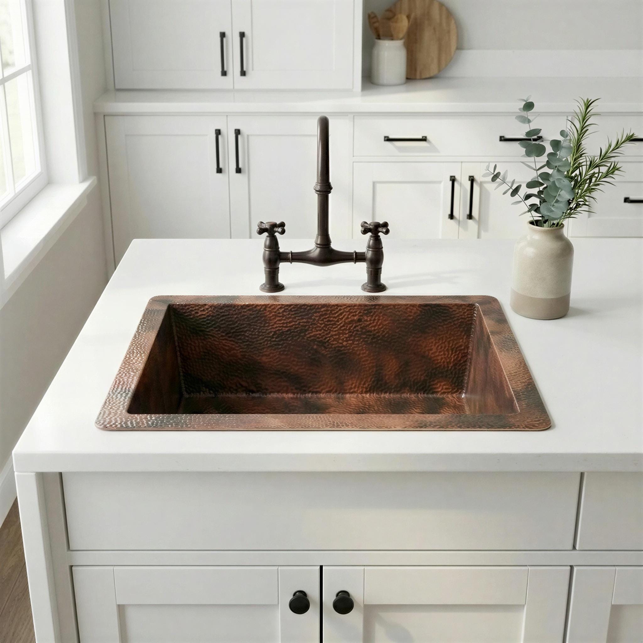 Copper kitchen sink on a white countertop with white cabinets and a window in the background.