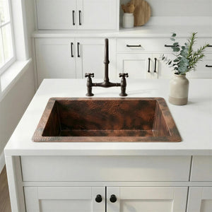 Copper kitchen sink on a white countertop with white cabinets and a window in the background.