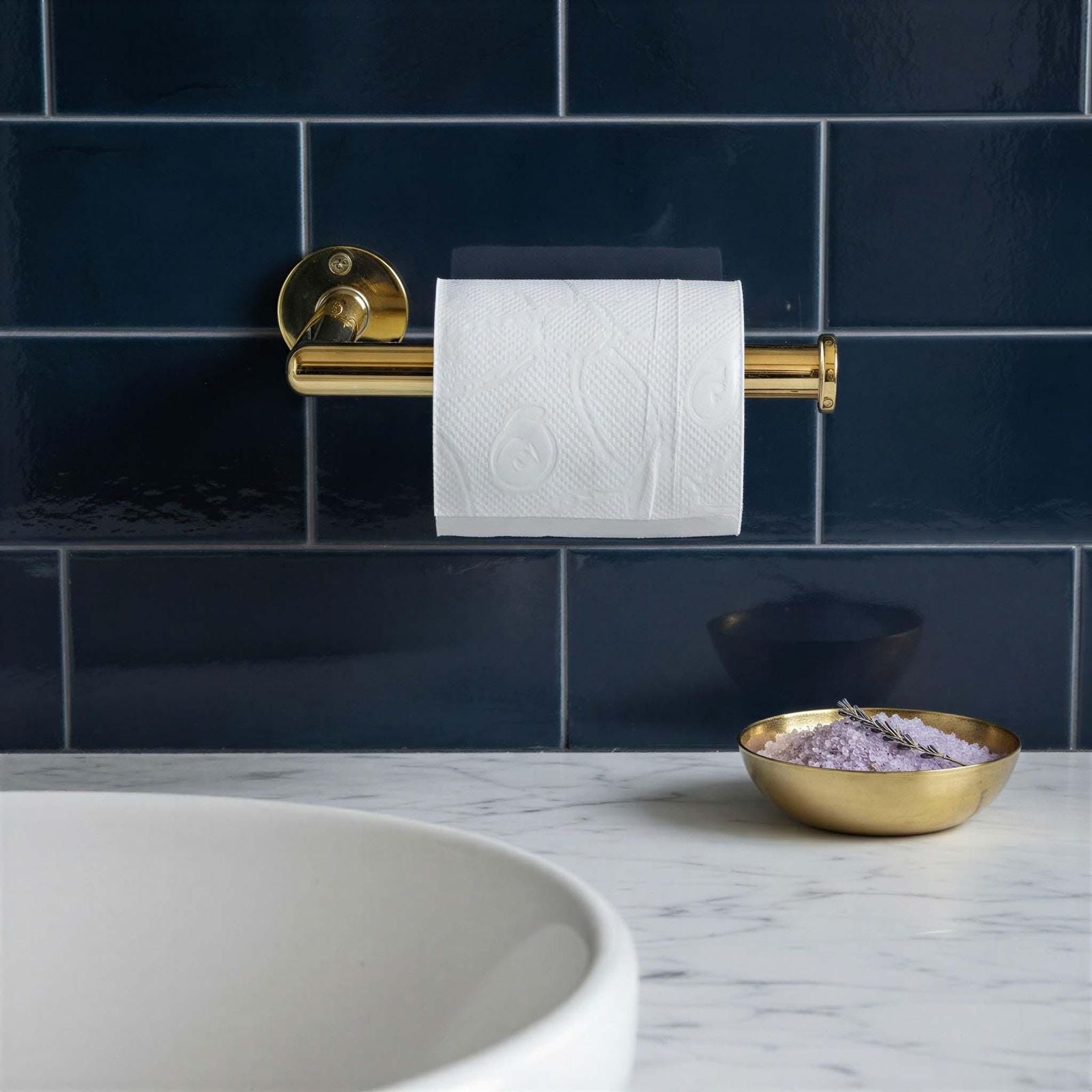 Gold toilet paper holder with white roll against a navy tiled wall.