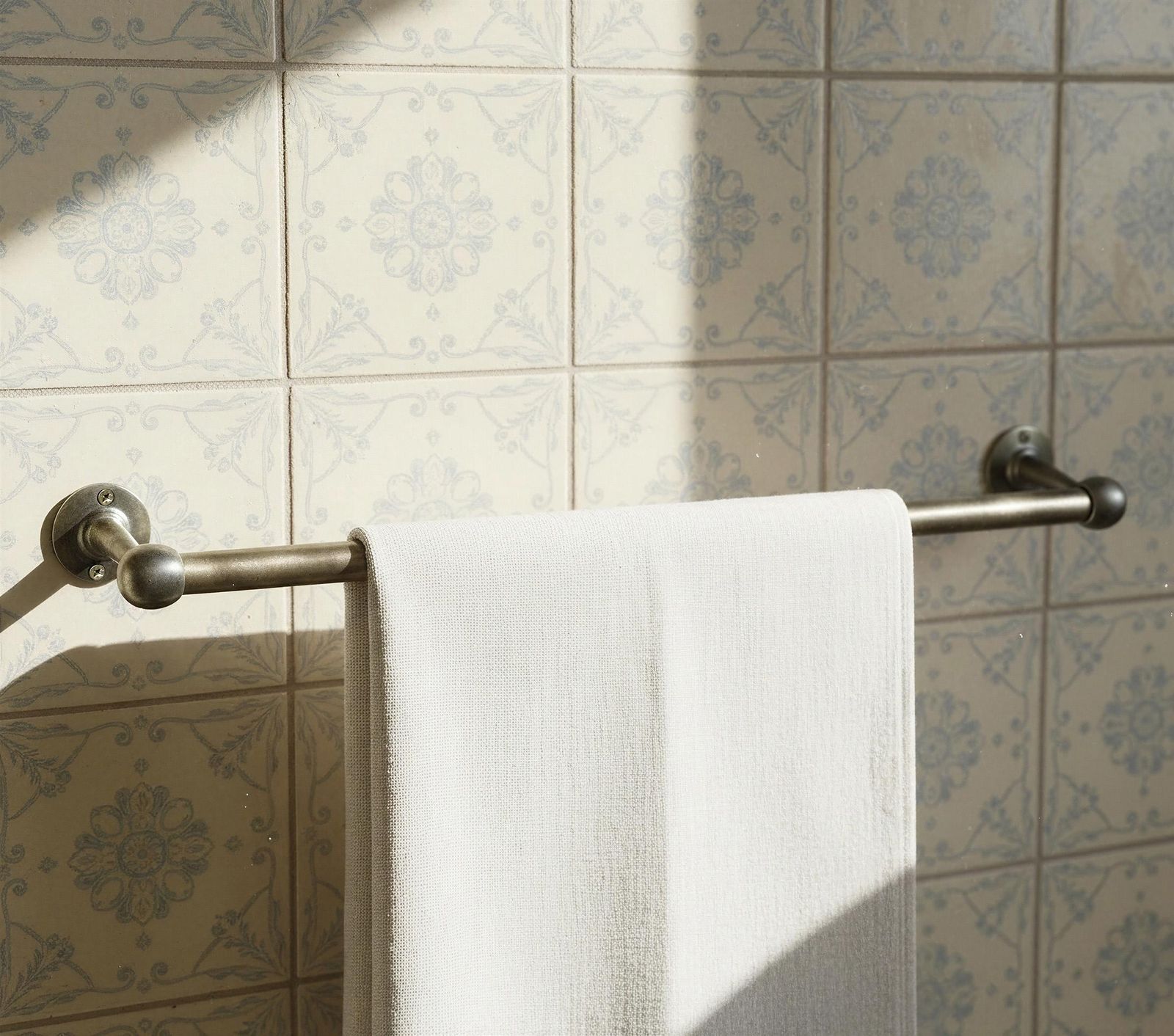 White towel hanging on a towel rack against a tiled bathroom wall.