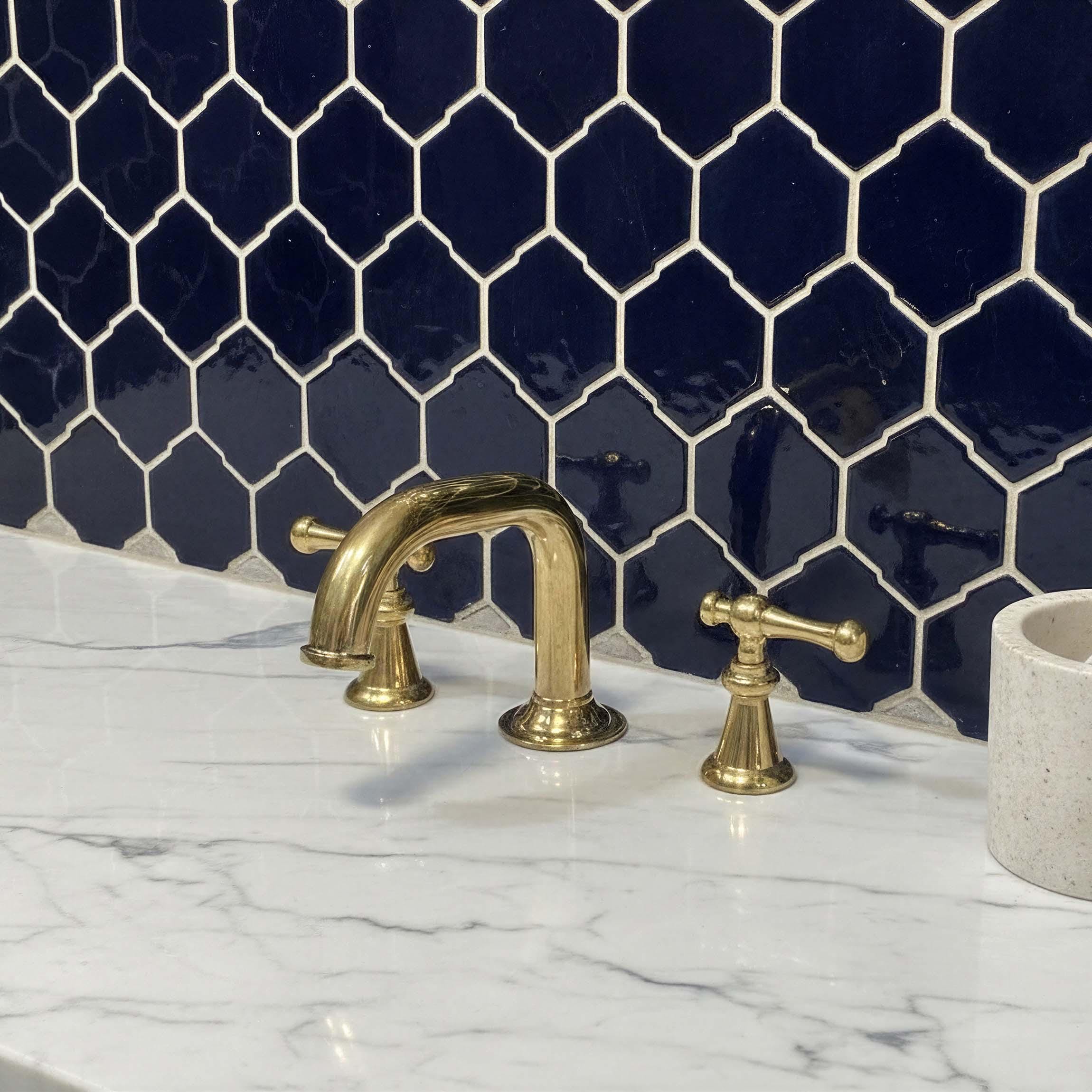 Gold faucet and handles on a marble countertop with a navy blue tiled wall.