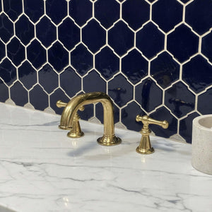 Gold faucet and handles on a marble countertop with a navy blue tiled wall.