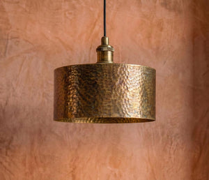 Hammered bronze pendant light against a textured brown wall