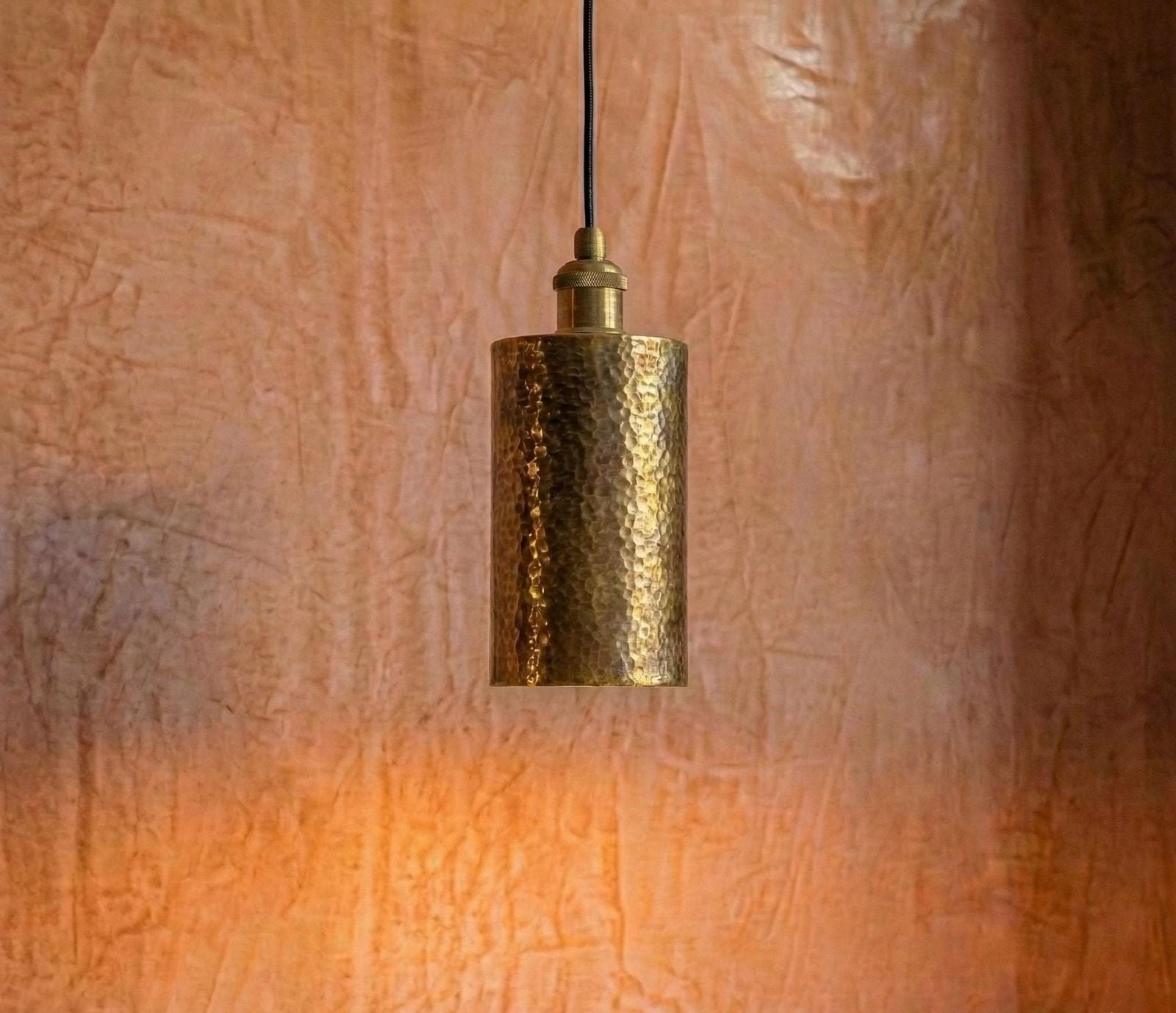 Gold pendant light hanging against a textured brown wall