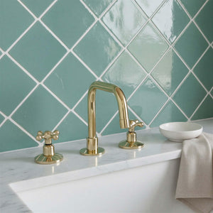 Gold faucet and handles on a white sink with green tiled wall