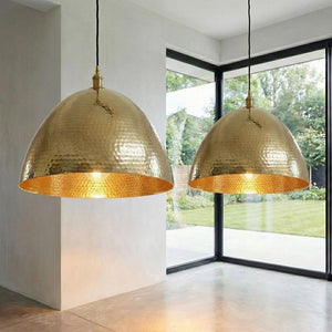 Luxury gold hanging light with a heavily textured surface, suspended by a black cord near a floor-to-ceiling glass window.