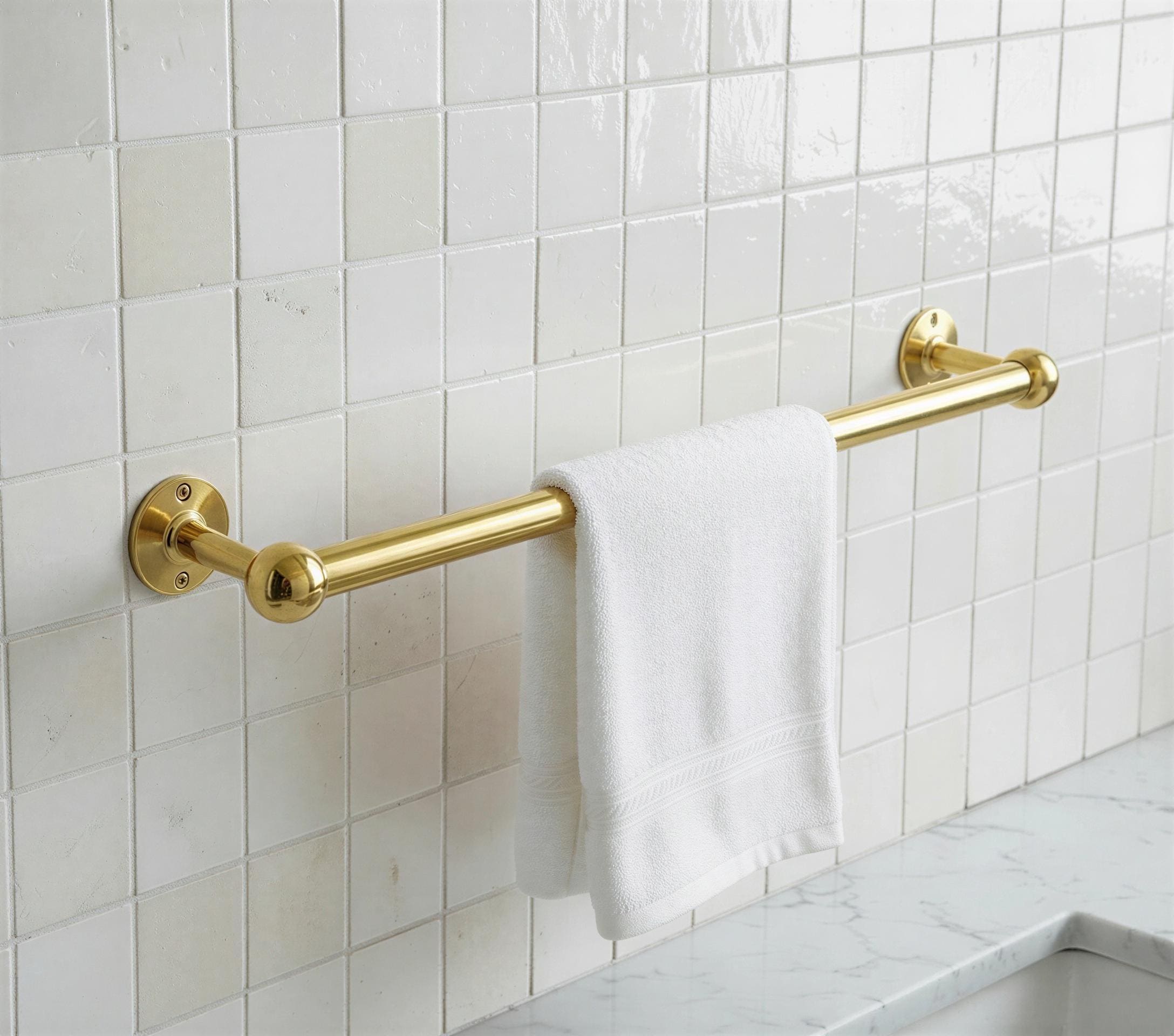 Gold towel rack with a white towel against a tiled bathroom wall.
