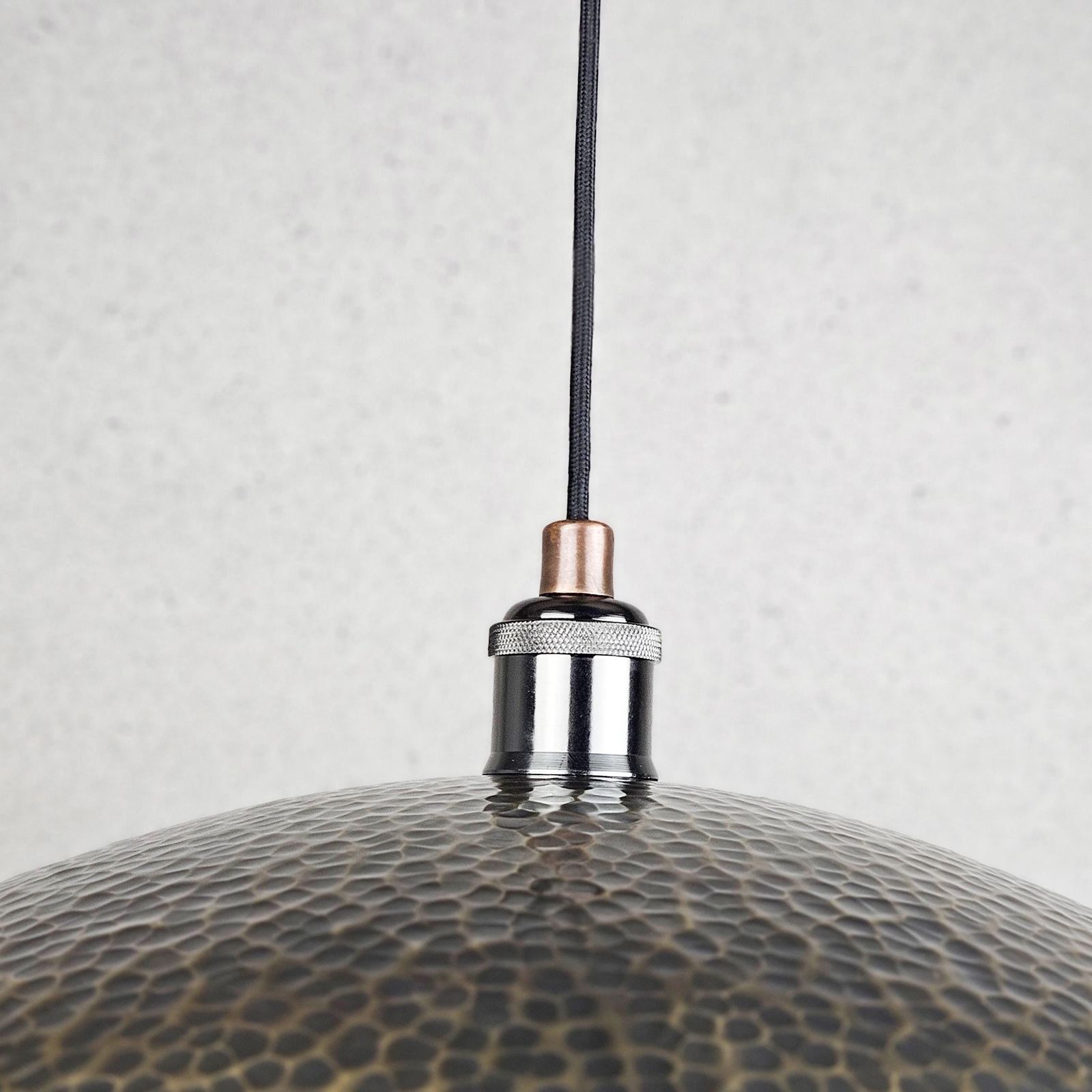 Close-up of a textured pendant light with a metallic finish on a neutral background
