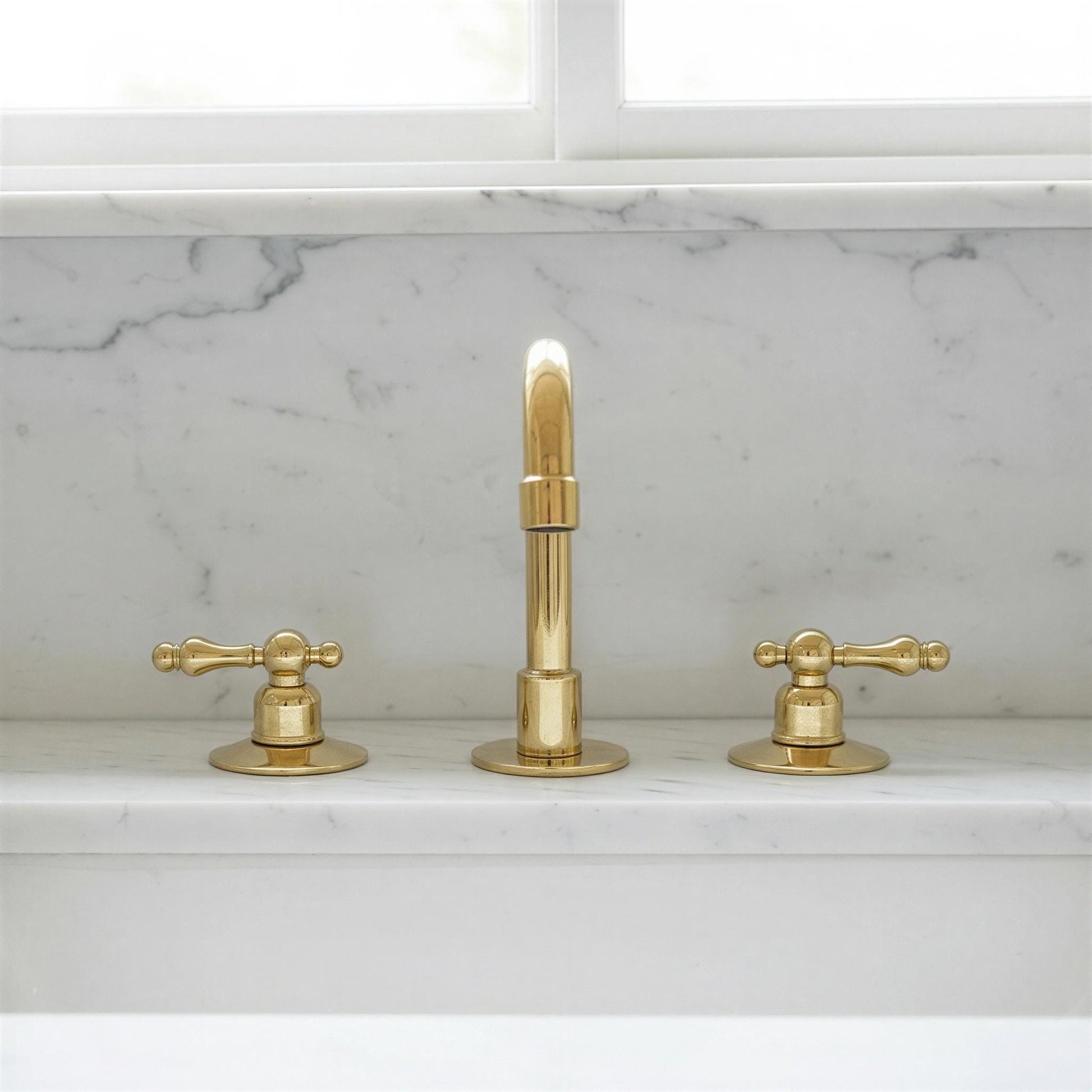 Gold faucet set on a marble countertop with a window in the background