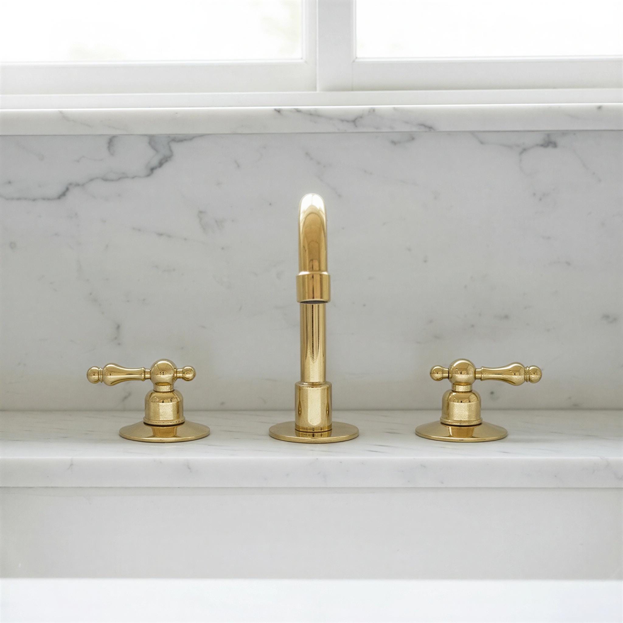 Gold faucet set on a marble countertop with a window in the background