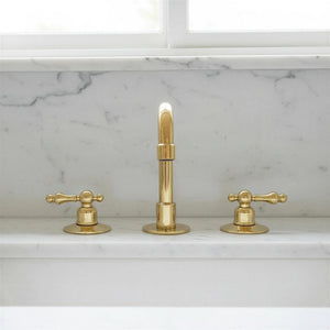 Gold faucet set on a marble countertop with a window in the background