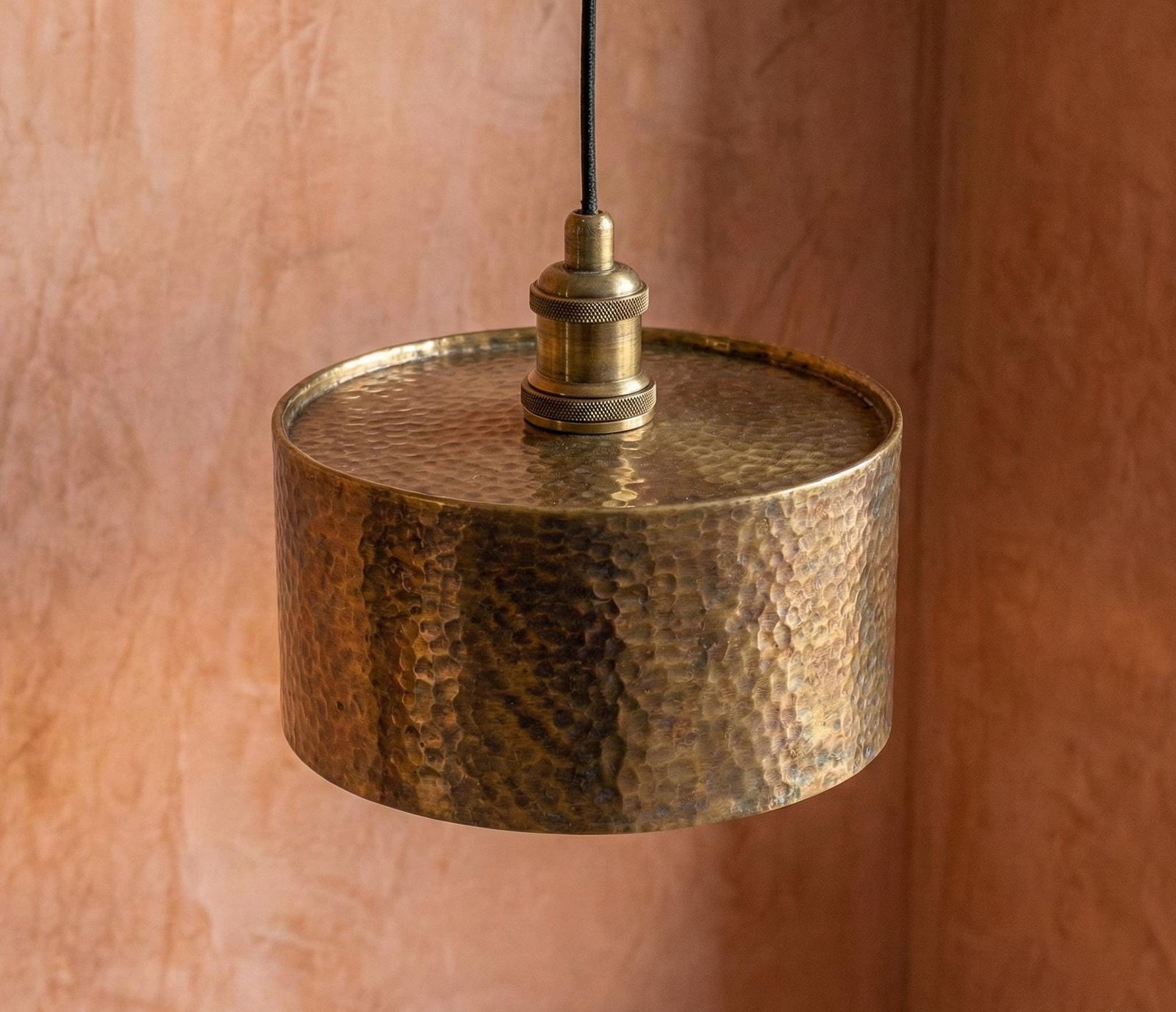 Hammered brass pendant light against a pinkish-brown background