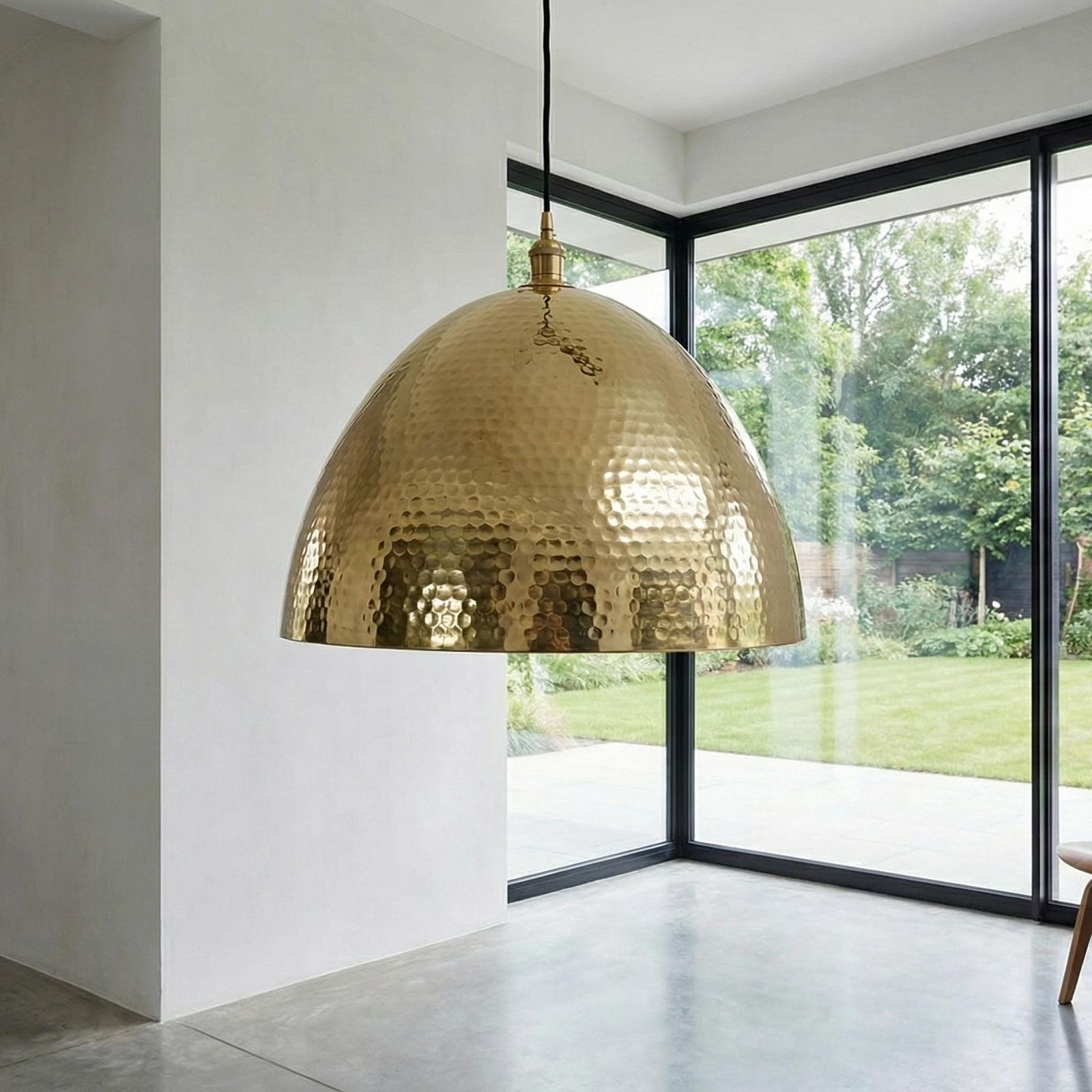 Close-up of a dimpled metallic bell ceiling lamp casting a warm glow from its interior bulb against a bright white wall.