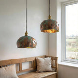 Two copper pendant lights hanging above a wooden bench with pillows in a room with a window.