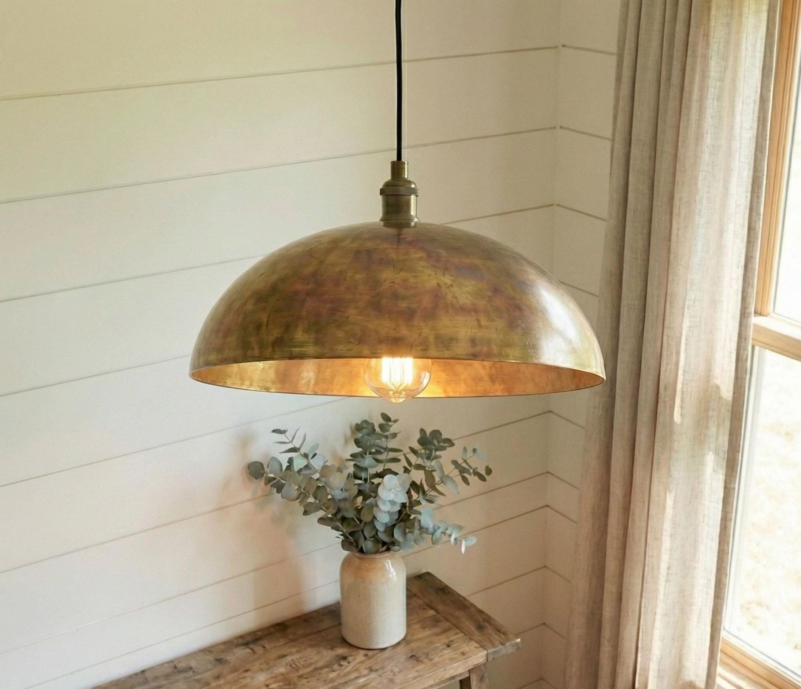 Brass pendant light hanging above a wooden surface with a vase of greenery.