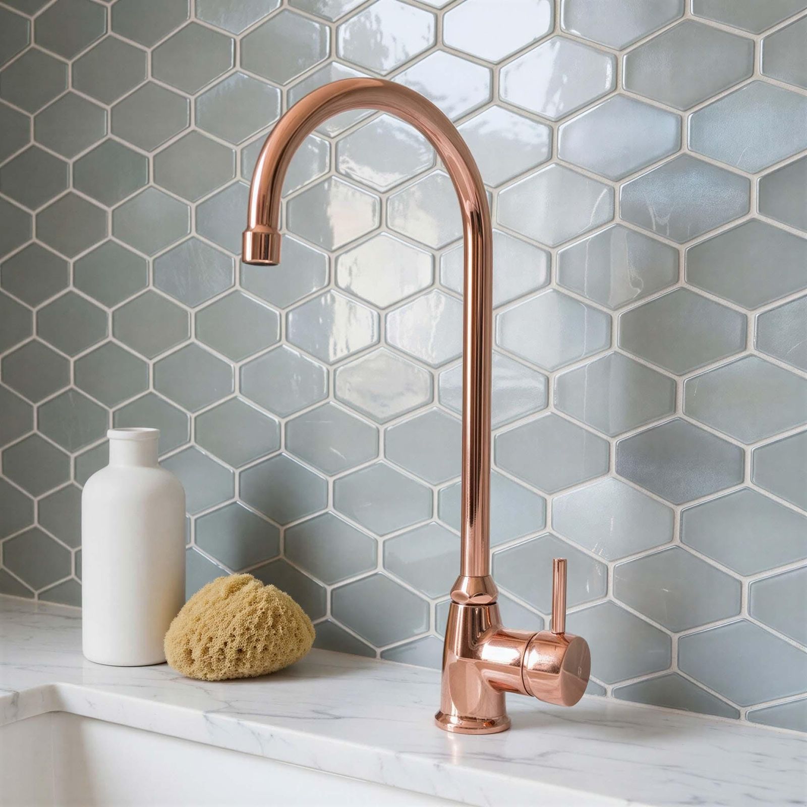 Rose gold faucet on a kitchen sink with hexagonal tiled wall
