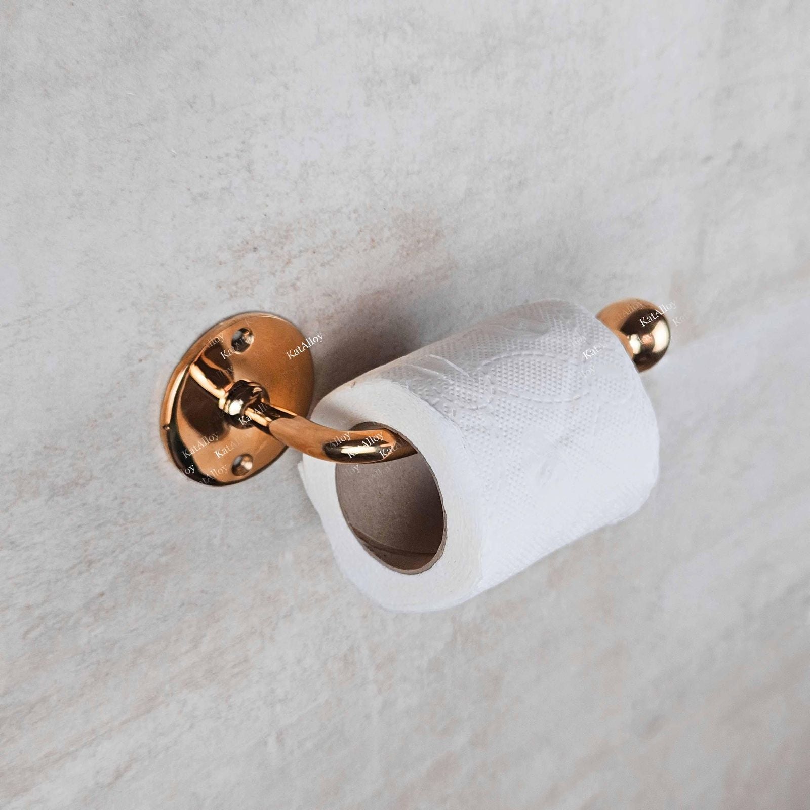 Rose gold toilet paper holder with a roll of toilet paper on a marble wall.