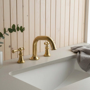 Gold faucet on a white sink with a wooden panel background